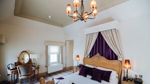 A hotel room with a large bed, a wooden headboard, a chandelier, a desk with a chair, and a window with curtains. - The Lynnhurst Hotel (Johnstone)