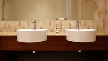 A bathroom with two white sinks, a mirror, and a tiled wall.
