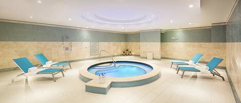 A spa area with a hot tub, lounge chairs, and tiled walls.