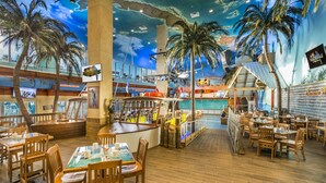 Un restaurant avec des tables et des chaises en bois, un coin bar et une fresque murale représentant une scène de plage.