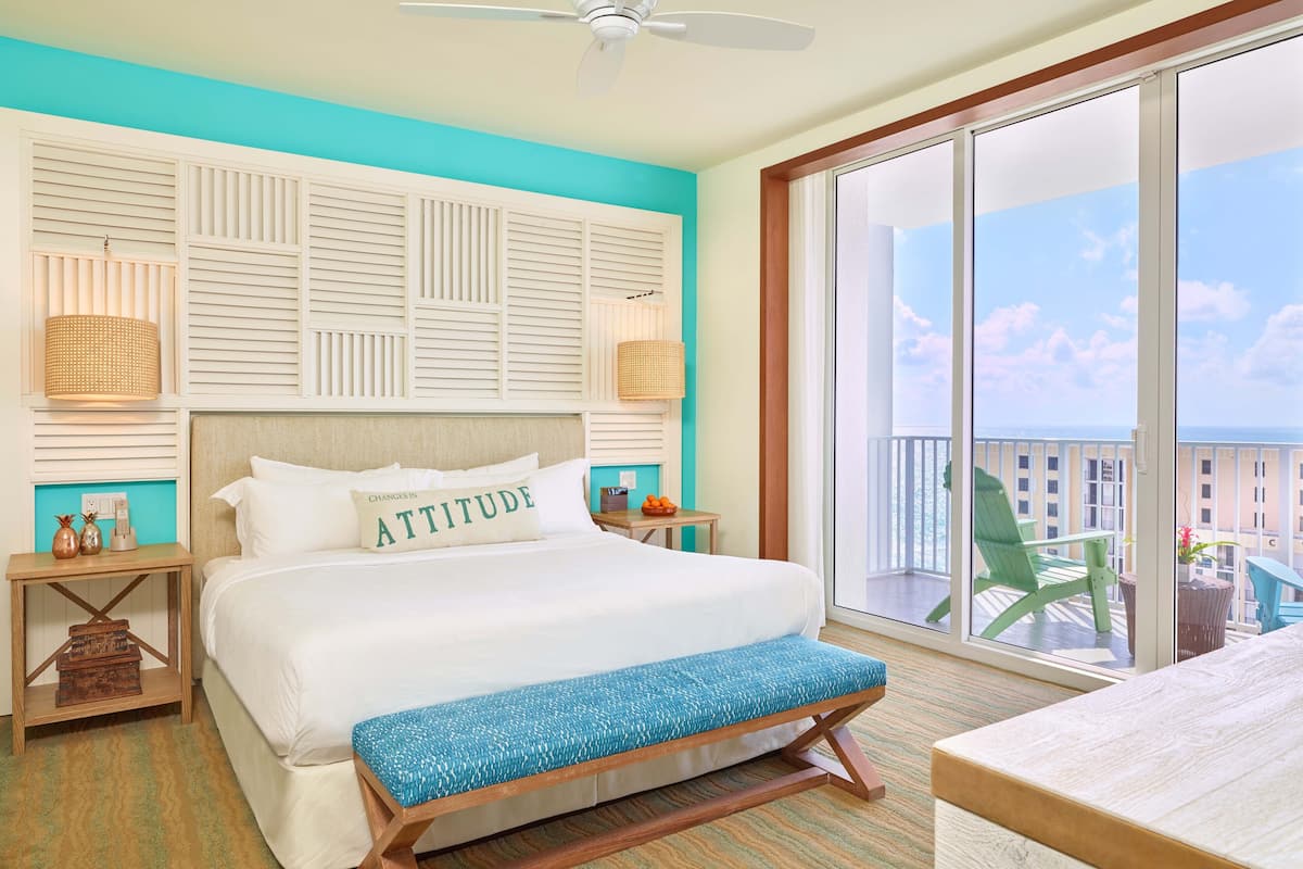 Une chambre d’hôtel avec un grand lit, un banc, un ventilateur de plafond et un balcon offrant une vue sur la ville.