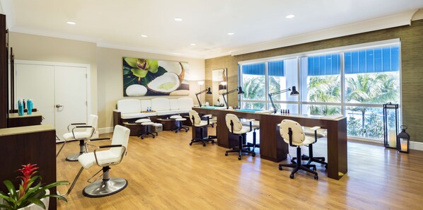 Un salón moderno con varias sillas, un mostrador de recepción y grandes ventanales con vista a palmeras.