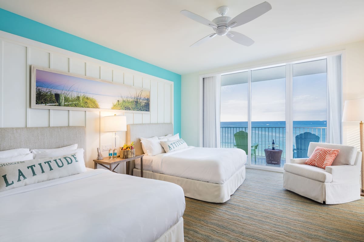 Une chambre d’hôtel avec deux lits, un ventilateur de plafond, une grande fenêtre donnant sur un beau paysage et une chaise avec un coussin.