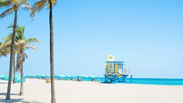 A beach with palm trees, a lifeguard tower, and umbrellas.