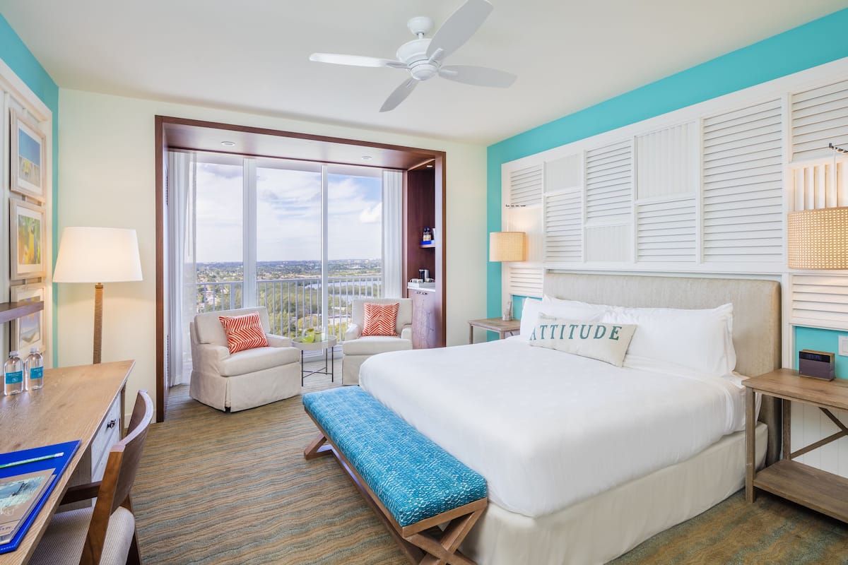 Une chambre d’hôtel avec un grand lit, un bureau, une chaise, un balcon avec vue et un ventilateur de plafond.