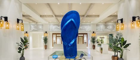 A modern lobby with a central blue sculpture, potted plants, and a high ceiling with exposed beams.