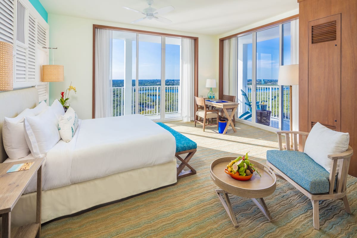 Une chambre d’hôtel avec un grand lit, un balcon avec une table et des chaises, et une vue sur la ville.