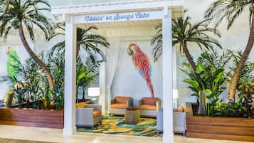 Vestíbulo con temática tropical, que presenta palmeras, un mural colorido y una zona de estar con dos sofás y una mesa de centro.