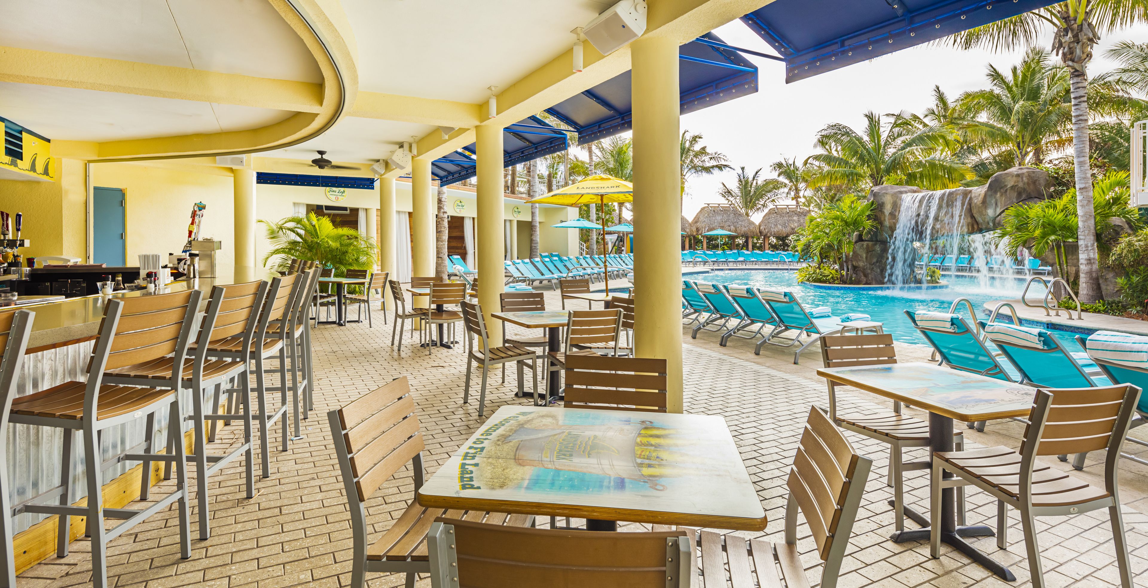 A poolside area with lounge chairs, tables, and a waterfall.