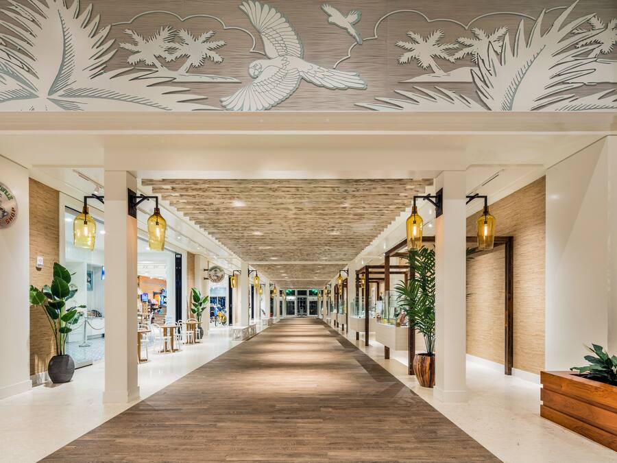 A hotel corridor with a wooden floor, modern lighting, and decorative ceiling artwork.