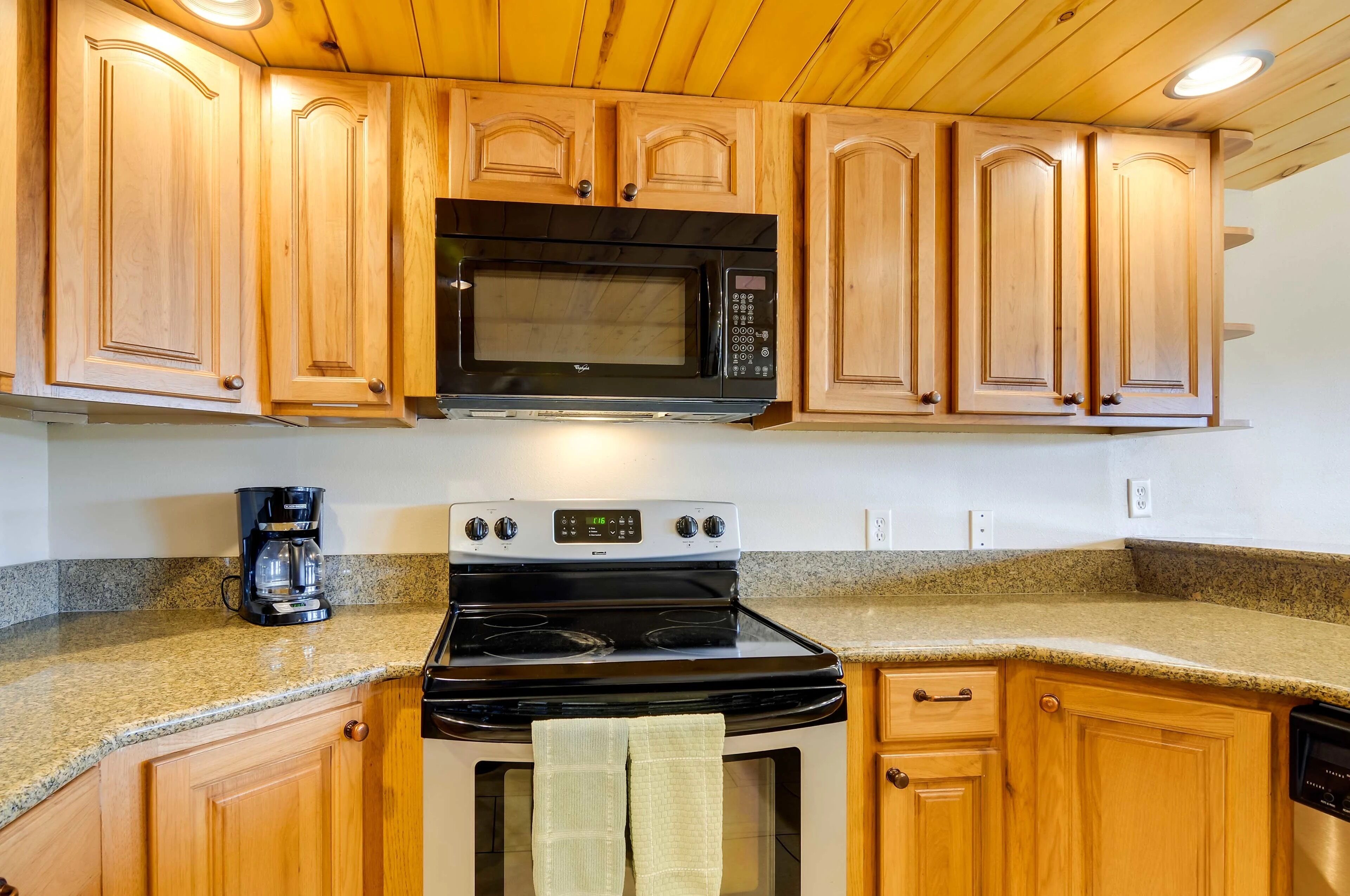 A kitchen with wooden cabinets, a microwave, a stove, and a coffee maker.