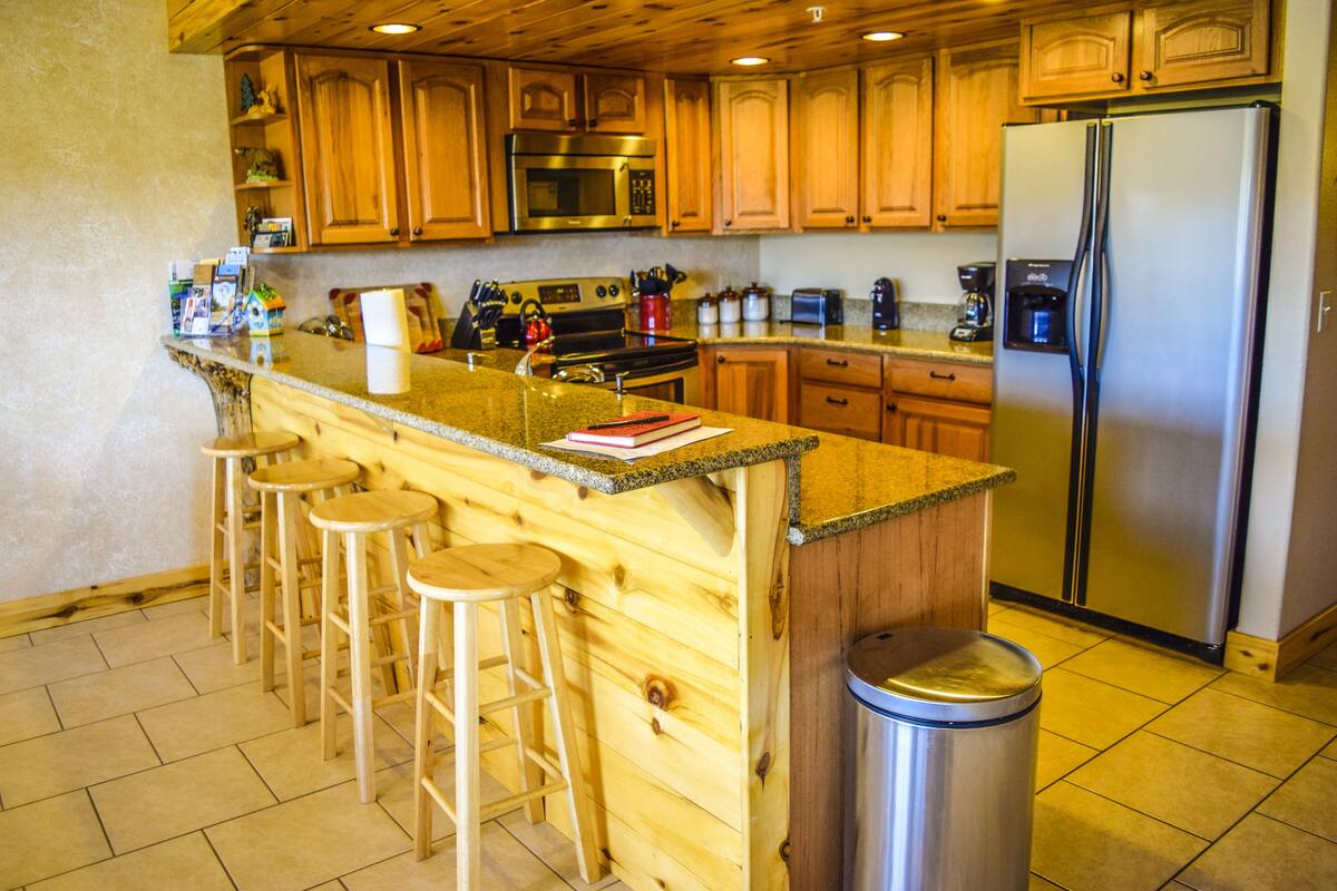 A kitchen with wooden cabinets, a stainless steel refrigerator, a granite countertop, and bar stools.