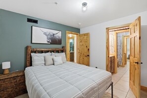A bedroom with a bed, wooden headboard, a framed picture, a nightstand, and a wooden door.