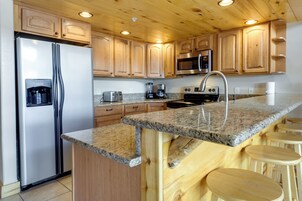 A kitchen with wooden cabinets, granite countertops, stainless steel appliances, and a bar area with stools.
