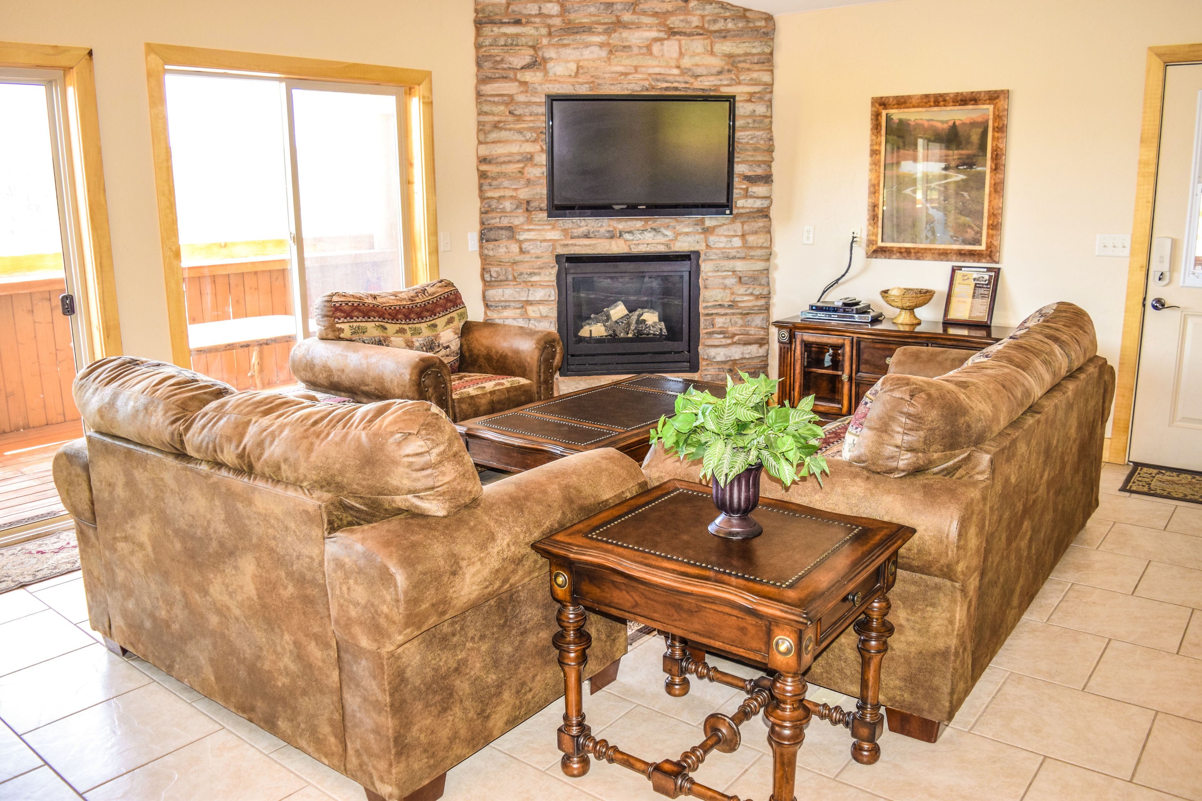 A living room with a stone fireplace, leather sofas, a wooden coffee table, and a flat-screen TV mounted above the fireplace.