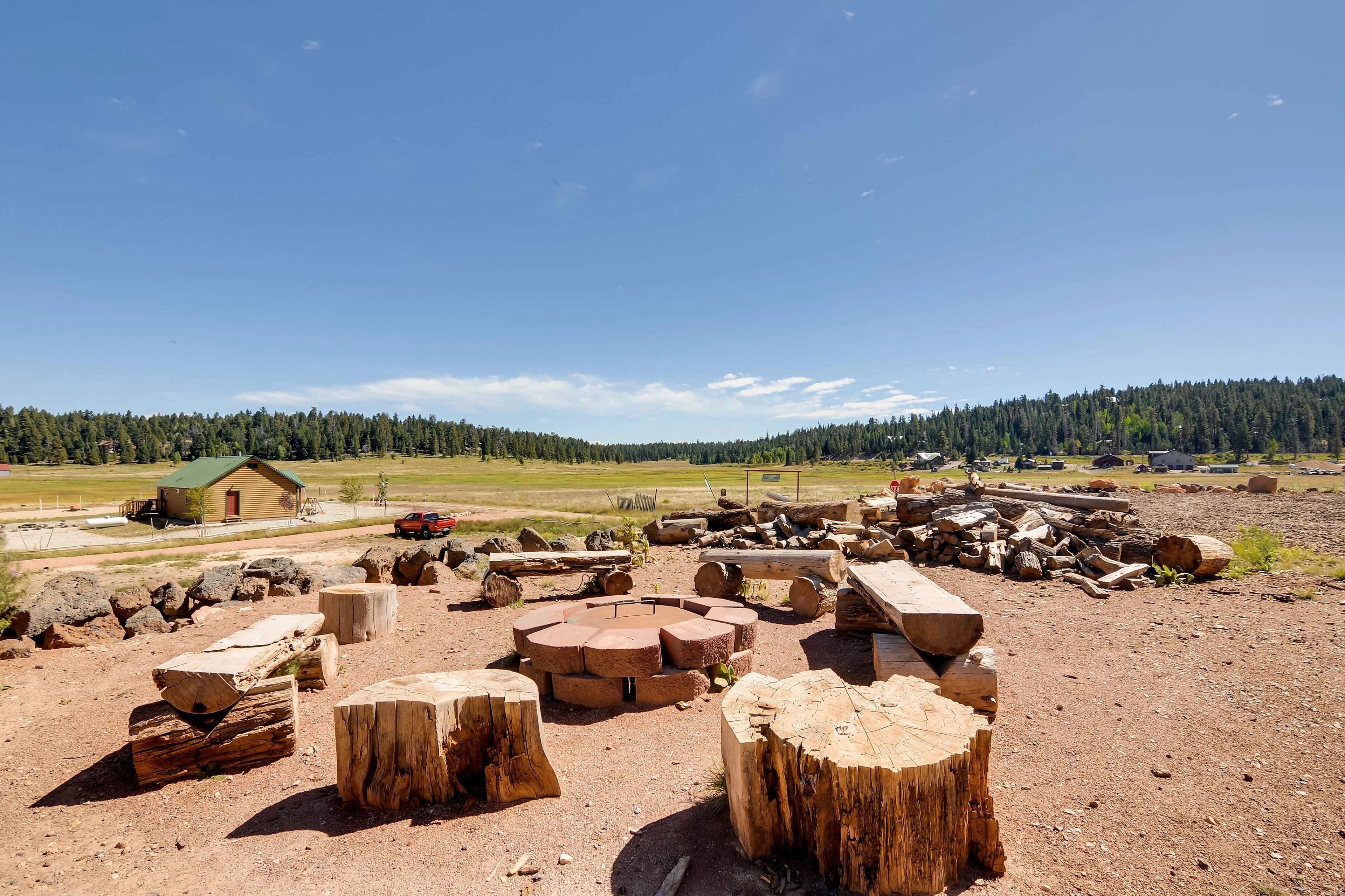 A rural landscape with a cabin, scattered logs, and a clear sky.
