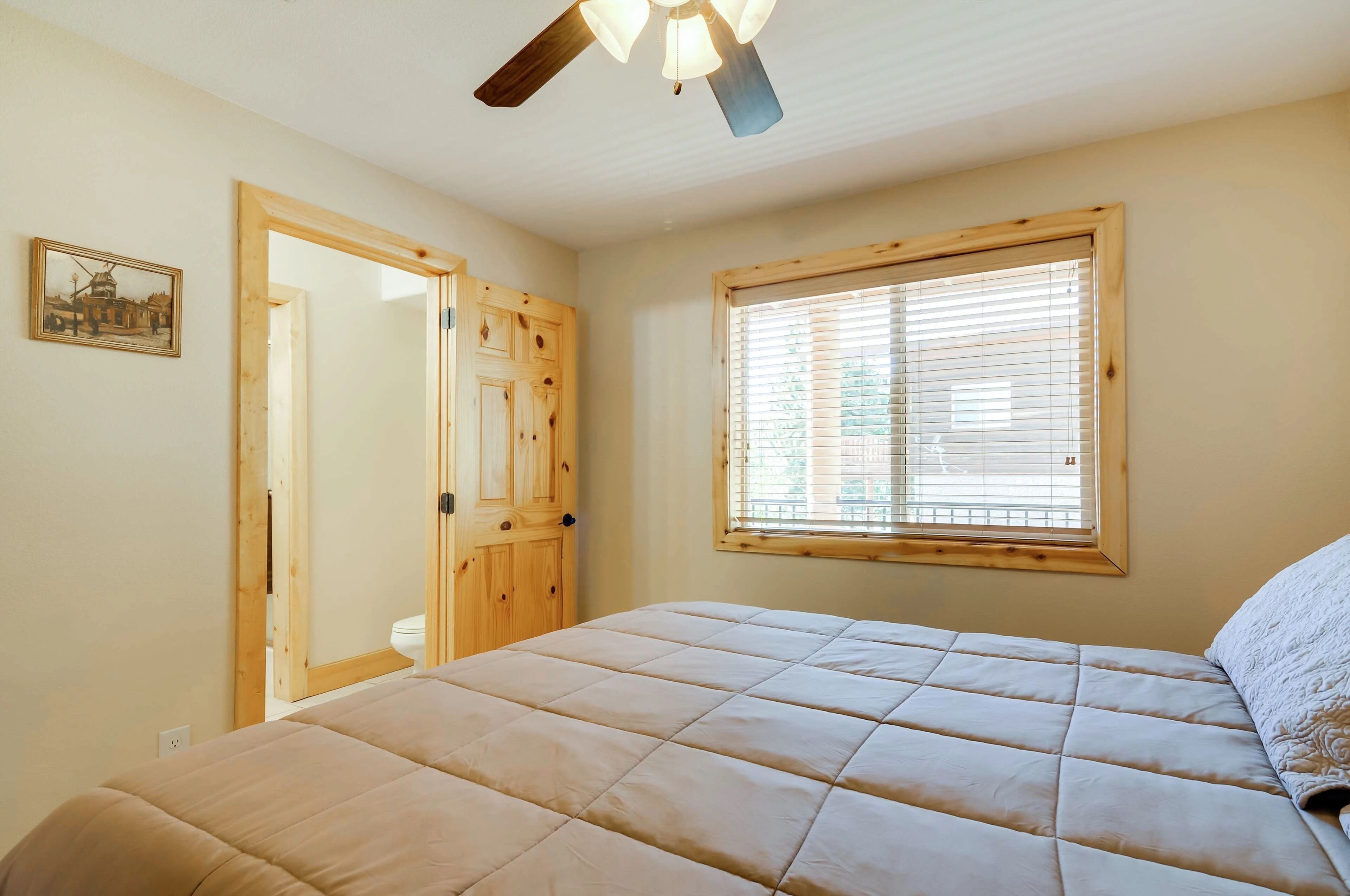 Un dormitorio con cama, ventana con persianas, ventilador de techo y puerta de madera.