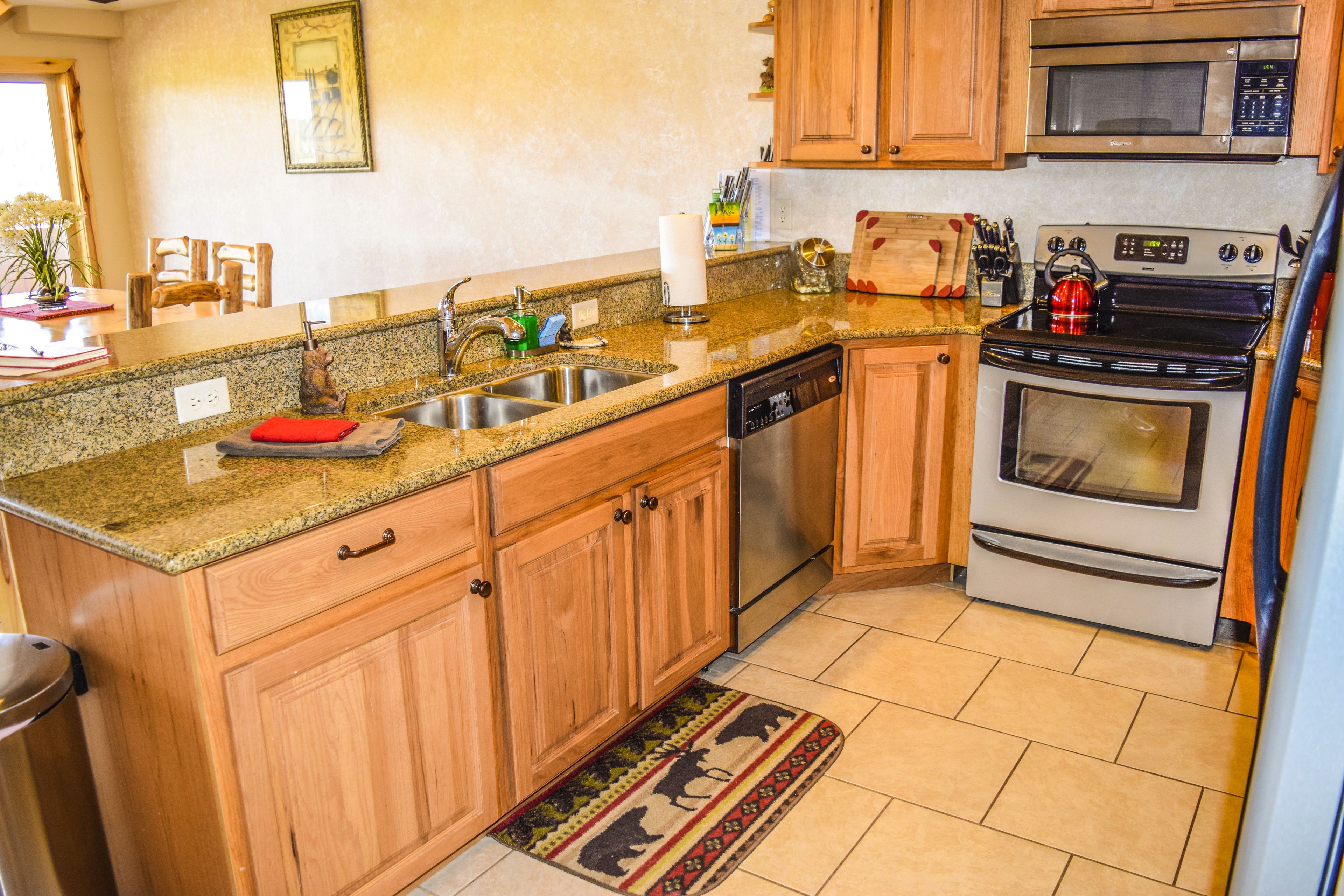 A kitchen with wooden cabinets, a stainless steel sink, a dishwasher, a microwave, an oven, and a red cutting board on the countertop.