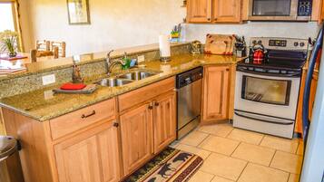 A kitchen with wooden cabinets, a stainless steel sink, a dishwasher, a microwave, an oven, and a red cutting board on the countertop.