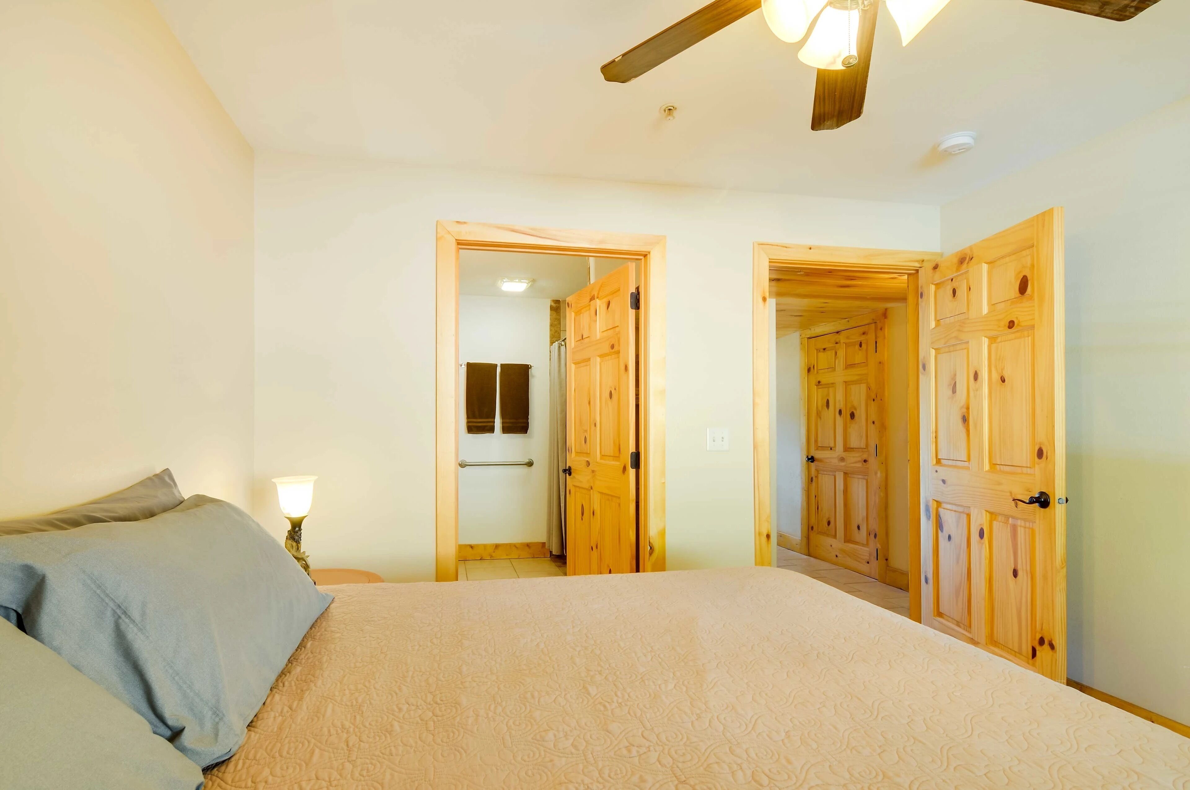 Une chambre à coucher avec un lit, une table de chevet et une lampe. Des portes en bois donnent accès aux autres pièces.