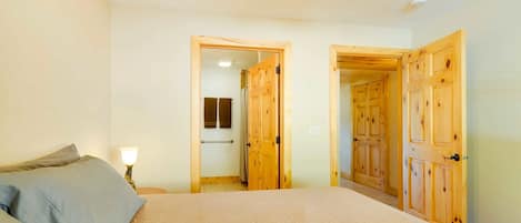 Un dormitorio con una cama, una mesita de noche y una lámpara. Hay puertas de madera que dan a otras habitaciones.