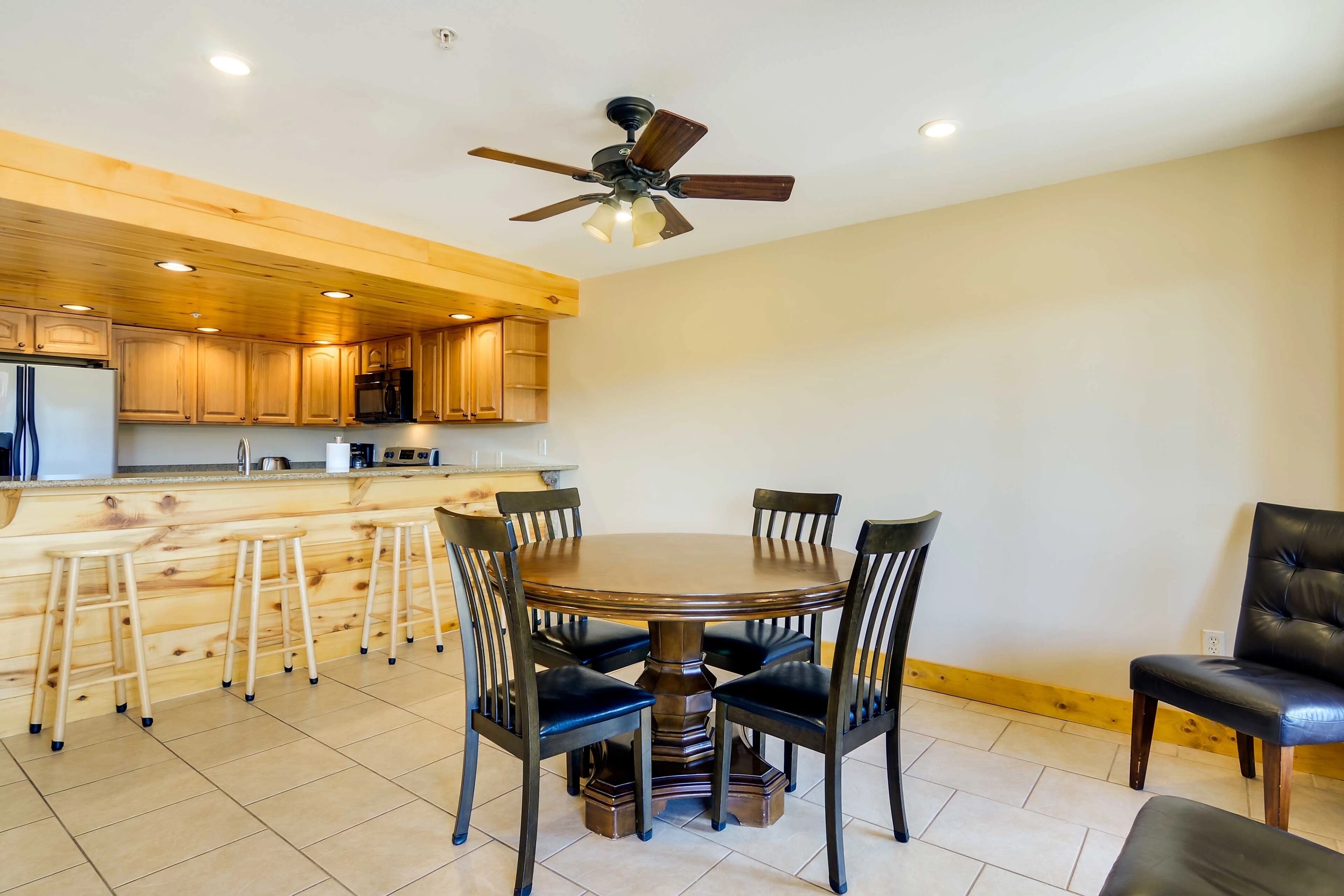 A modern kitchen with wooden cabinets, a central island, and a dining area with a round table and chairs.