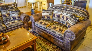 Een woonkamer met een zithoek, inclusief kussens met dessin, een houten salontafel en een vloerkleed.