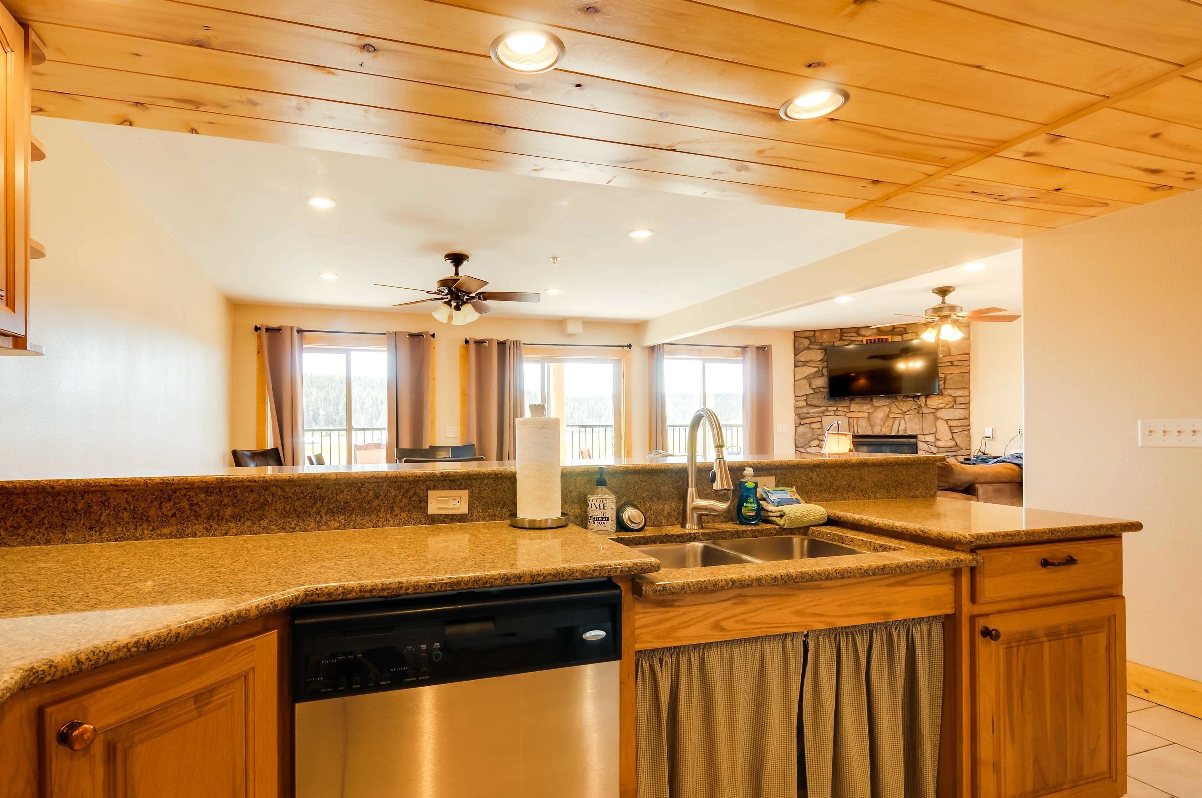 A kitchen with granite countertops, wooden cabinets, a dishwasher, a stone backsplash, and a ceiling fan.