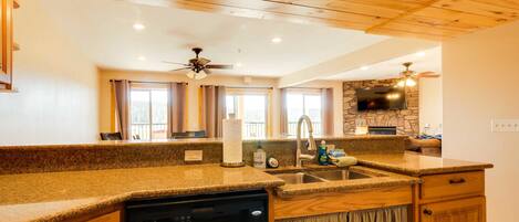 A kitchen with granite countertops, wooden cabinets, a dishwasher, a stone backsplash, and a ceiling fan.