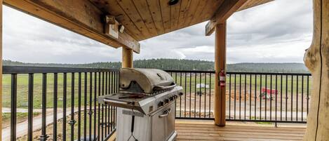A covered outdoor area with a barbecue grill, wooden deck, and a view of a road and trees.