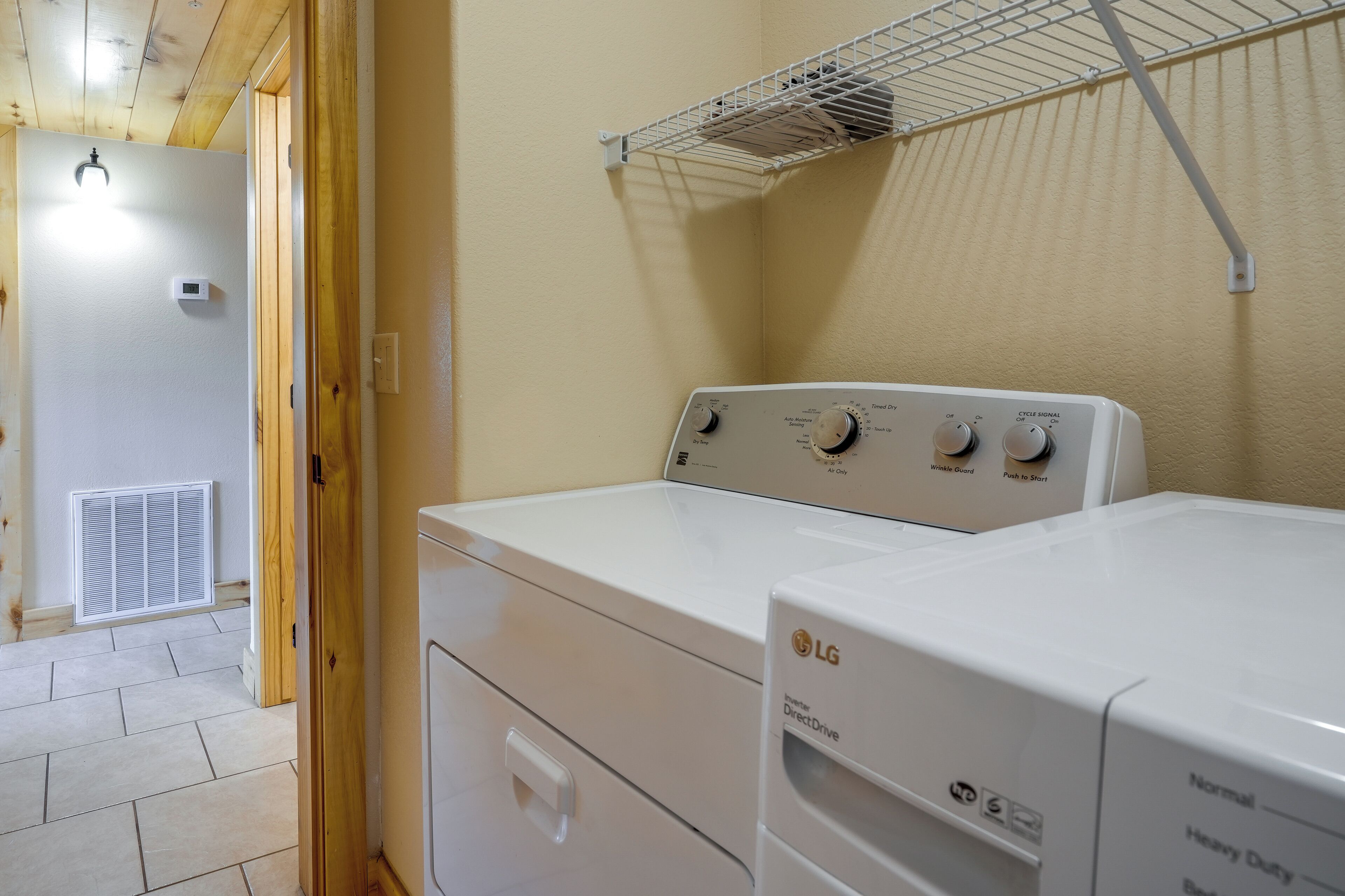 Un área de lavandería con dos lavadoras LG DirectDrive blancas, un tendedero metálico y un aire acondicionado con conductos de ventilación.