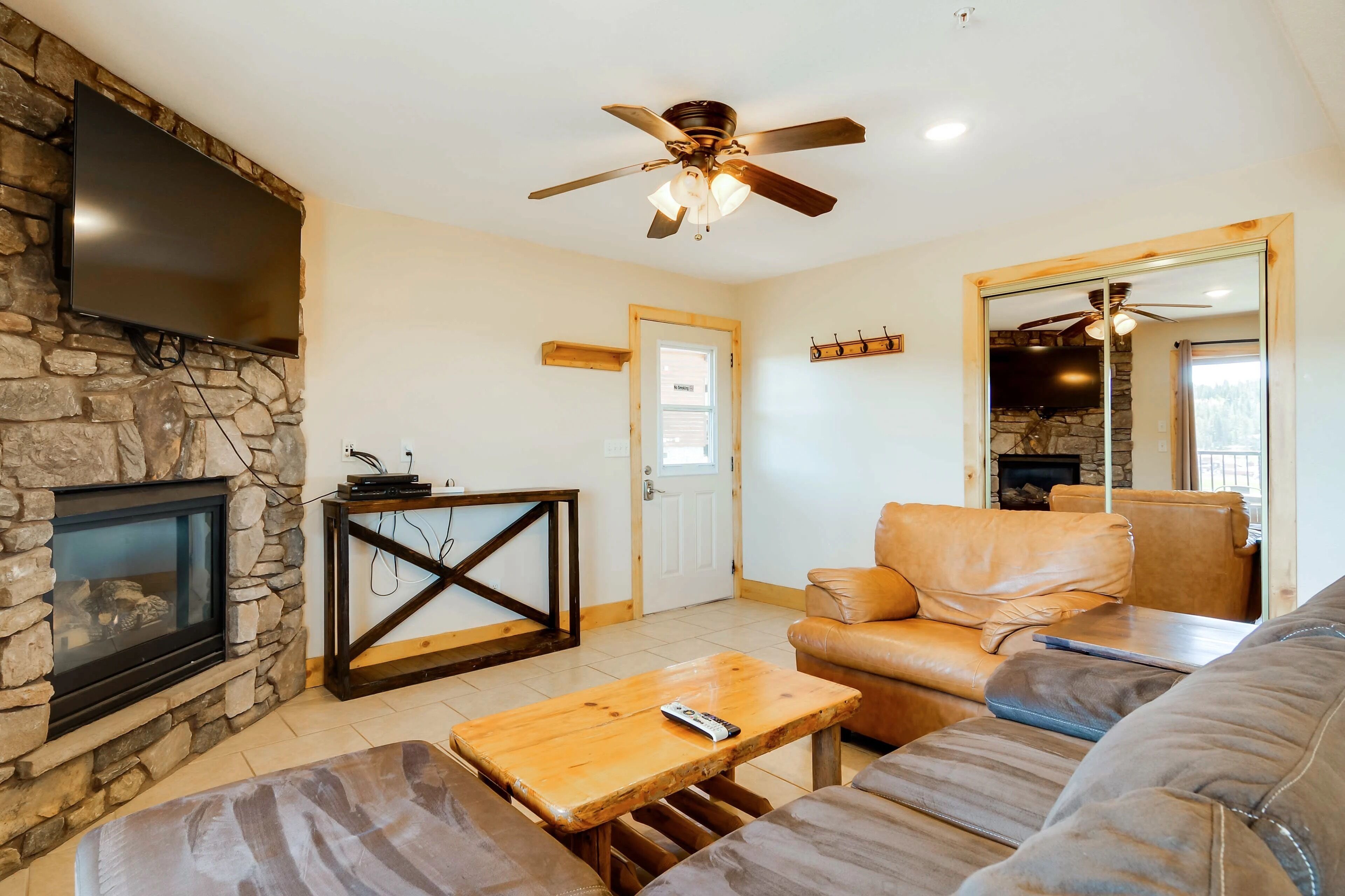 A living room with a stone fireplace, leather sofa, wooden coffee table, and a mounted TV.