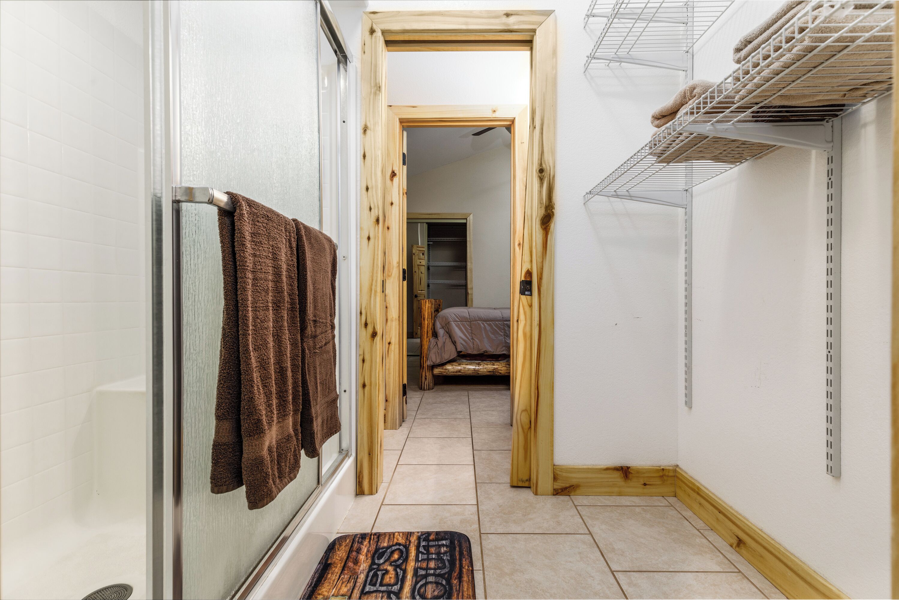 A narrow hallway with a shower, a wooden door, and a bed in the background.