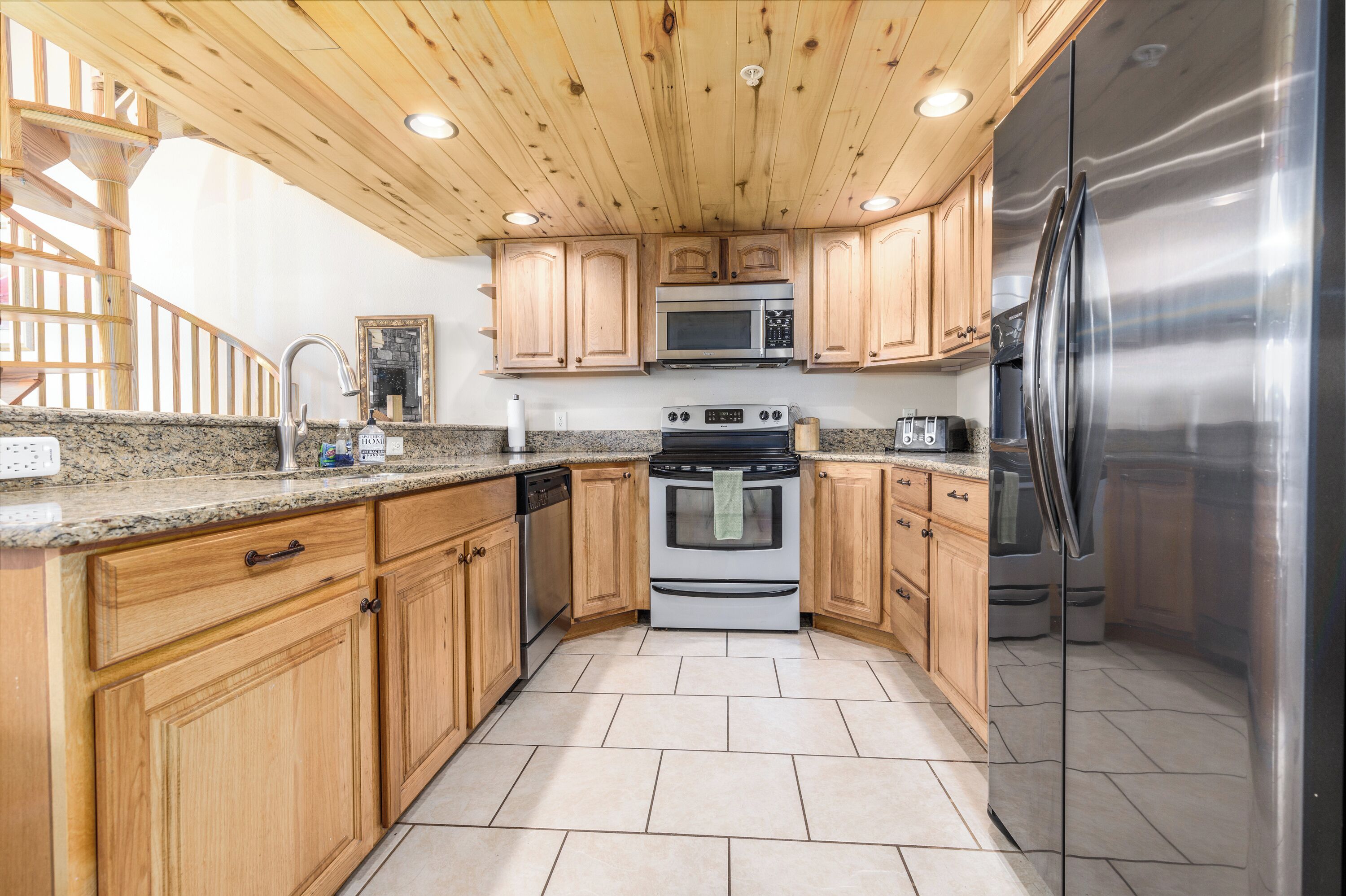 Una cocina con gabinetes de madera, encimeras de granito, electrodomésticos de acero inoxidable y techo de madera.