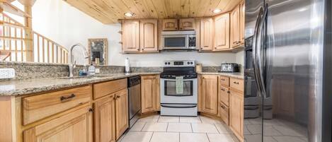 Una cocina con gabinetes de madera, encimeras de granito, electrodomésticos de acero inoxidable y techo de madera.
