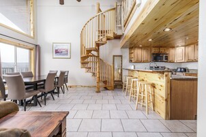 A modern kitchen with wooden cabinets, a stainless steel microwave, and a wooden spiral staircase.
