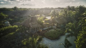 Un complexe hôtelier tropical doté de bâtiments aux toits de chaume, de palmiers et d’une plage de sable.