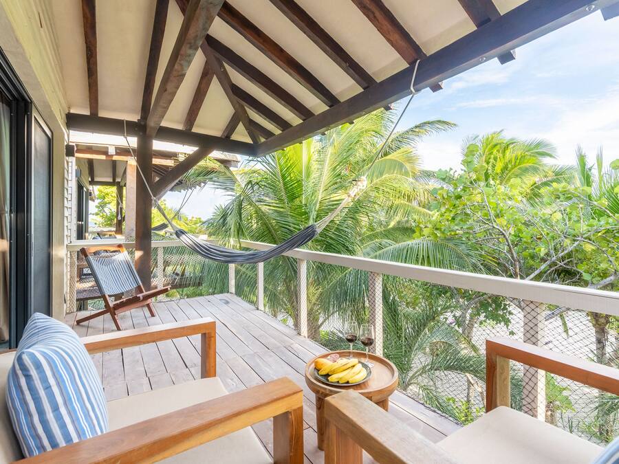 A wooden deck with a hammock, lounge chairs, and a table with a fruit bowl and glasses.