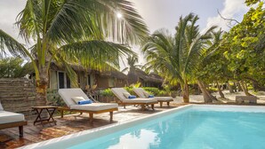 Un espace aménagé au bord de la piscine, avec des chaises longues et un bâtiment dont le toit est fait de chaume.