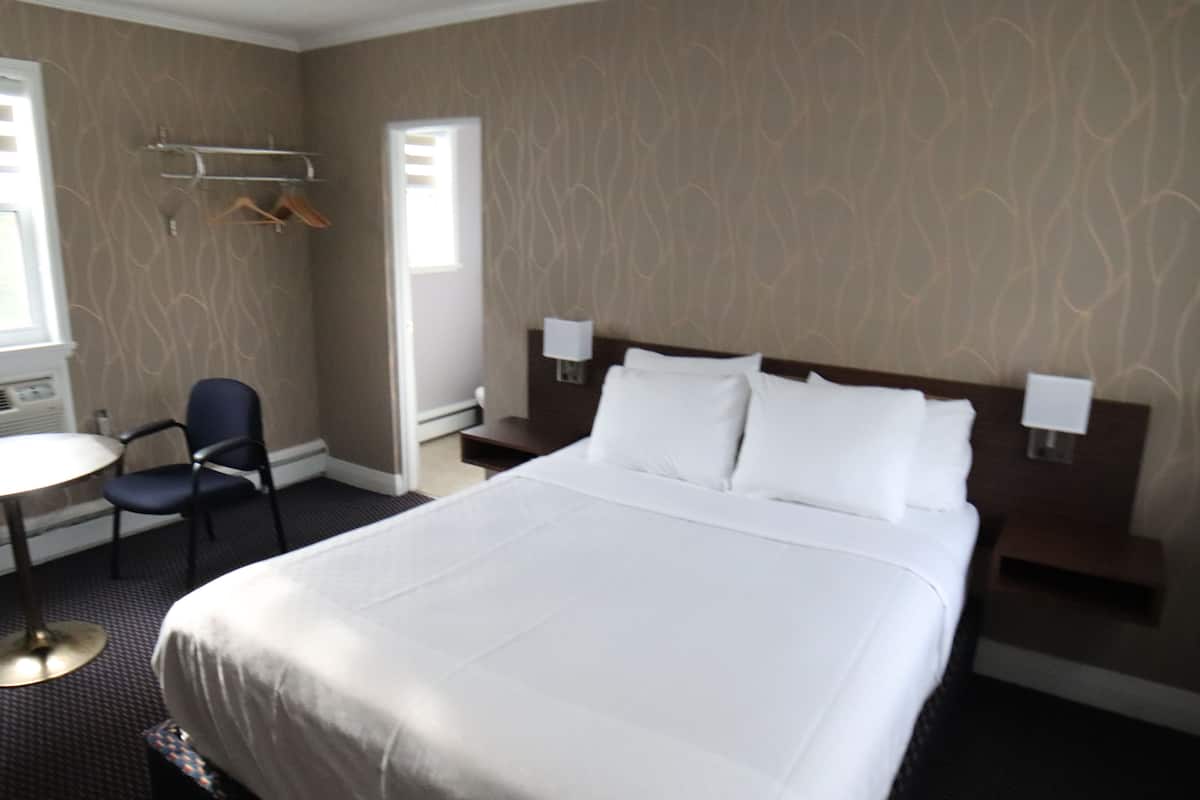 Ein Hotelzimmer mit einem großen Bett, einem Sessel, einem kleinen Tisch und einem Kleiderständer.