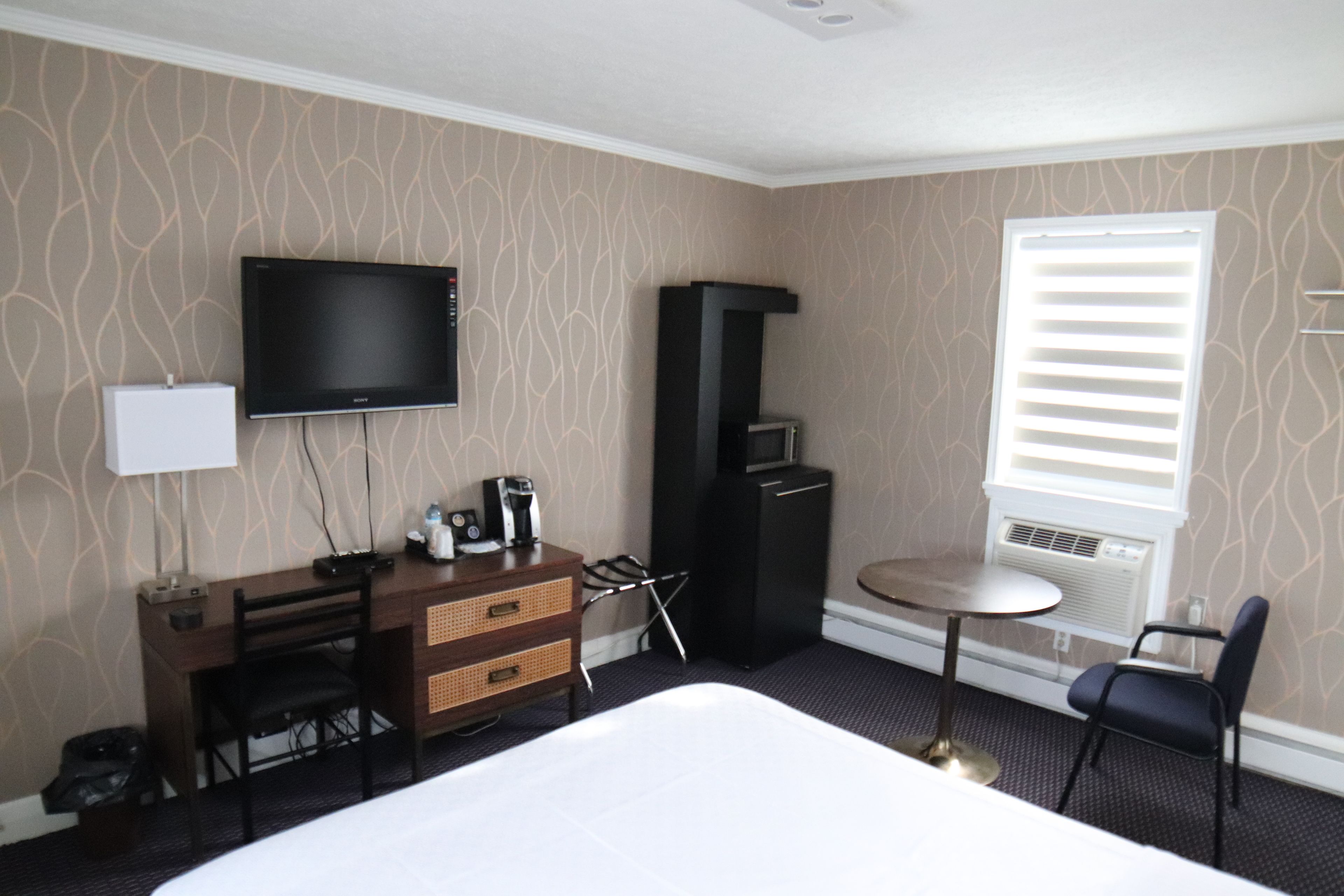 Habitación de hotel con una cama, un escritorio con televisor, una mesita y una silla.