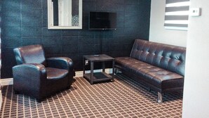 A living room with a dark wall, a brown leather sofa, a blue armchair, and a small table. - Walkerton Inn Motel (Brockton)
