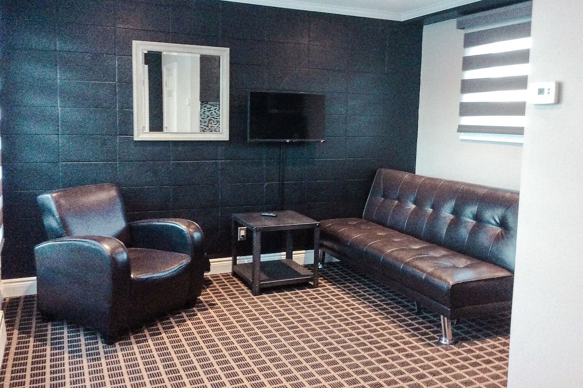 Ein Wohnzimmer mit dunkler Wand, einem braunen Ledersofa, einem blauen Sessel und einem kleinen Tisch.