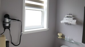A bathroom with a hairdryer, a shelf with toiletries, and a towel rack. - Walkerton Inn Motel (Brockton)