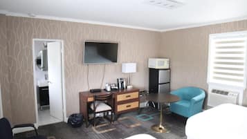 Una habitación de hotel con cama, escritorio con silla, televisión, microondas y ventana con persianas.