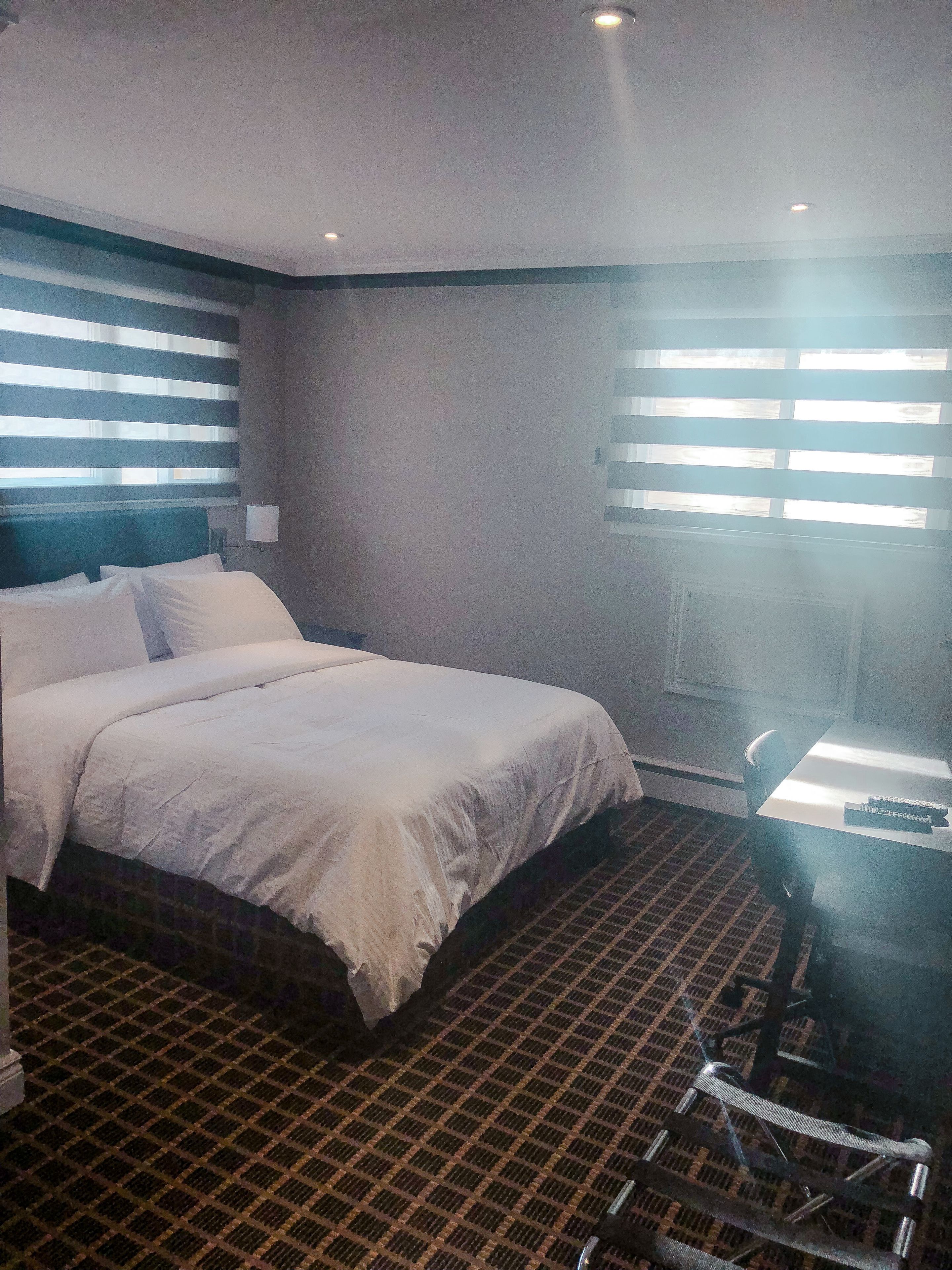 A hotel room with a large bed, a desk with a chair, and a window with blinds.