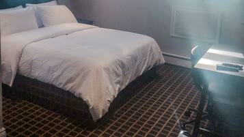 A hotel room with a large bed, a desk with a chair, and a window with blinds.