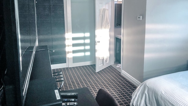 A hotel room with a large bed, a desk with a computer and remote controls, a shower area, and a view of the outside. - Walkerton Inn Motel (Brockton)