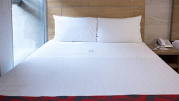 A hotel room with a large bed, a wooden headboard, a bedside phone, and a window with blinds.