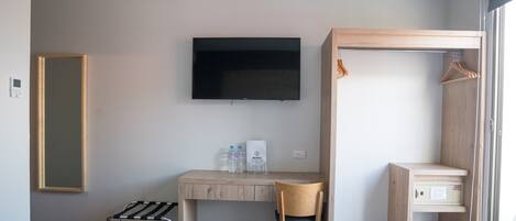 A hotel room with a bed, a desk with a chair, a television mounted on the wall, a coat rack, and a small cabinet.